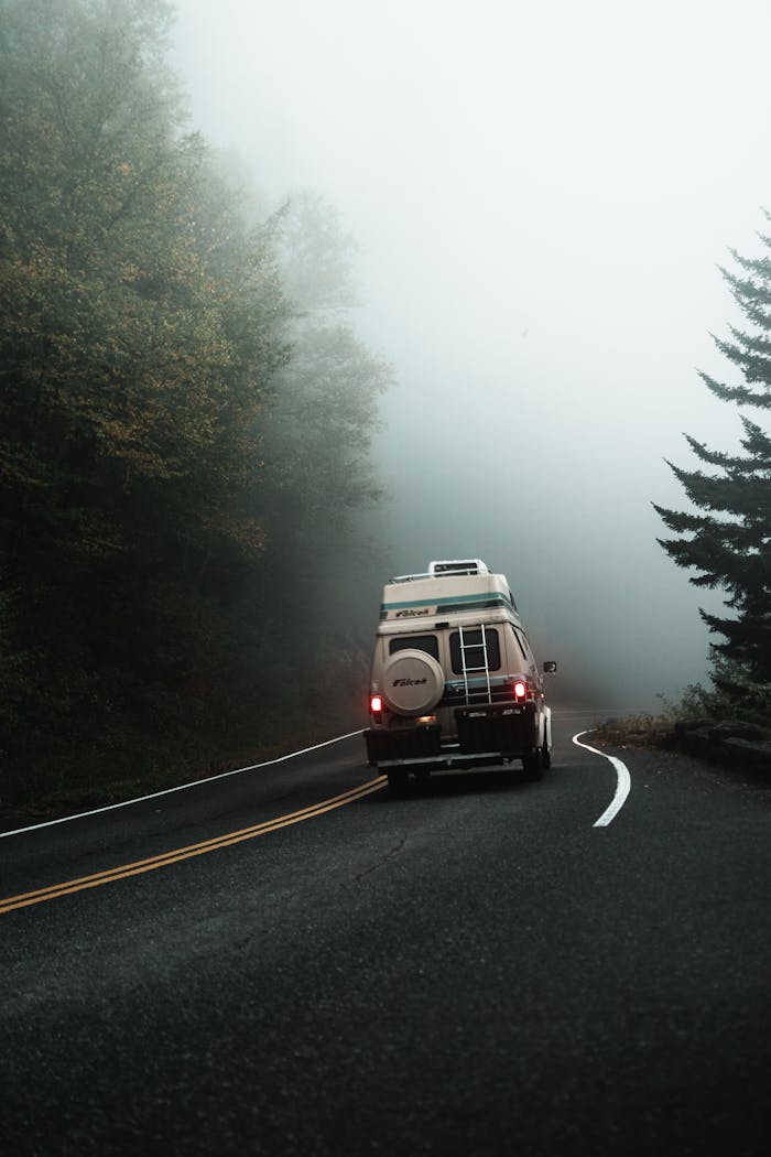 A camper van travels through a foggy rural road, creating a serene scene for adventure.